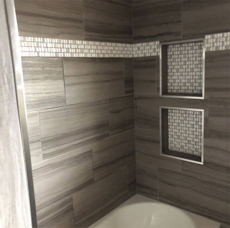 Bathroom with gray marbled tile, white mosaic accents, and recessed shelves.