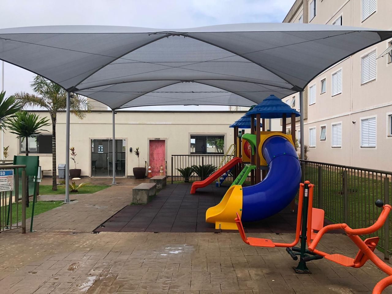 Um playground com escorregador e equipamentos de ginástica sob um guarda-sol.