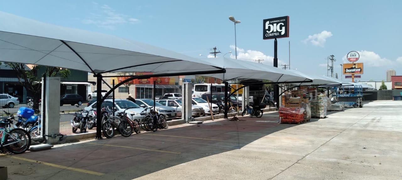 Um estacionamento com muitos carros e motos estacionados sob uma marquise.
