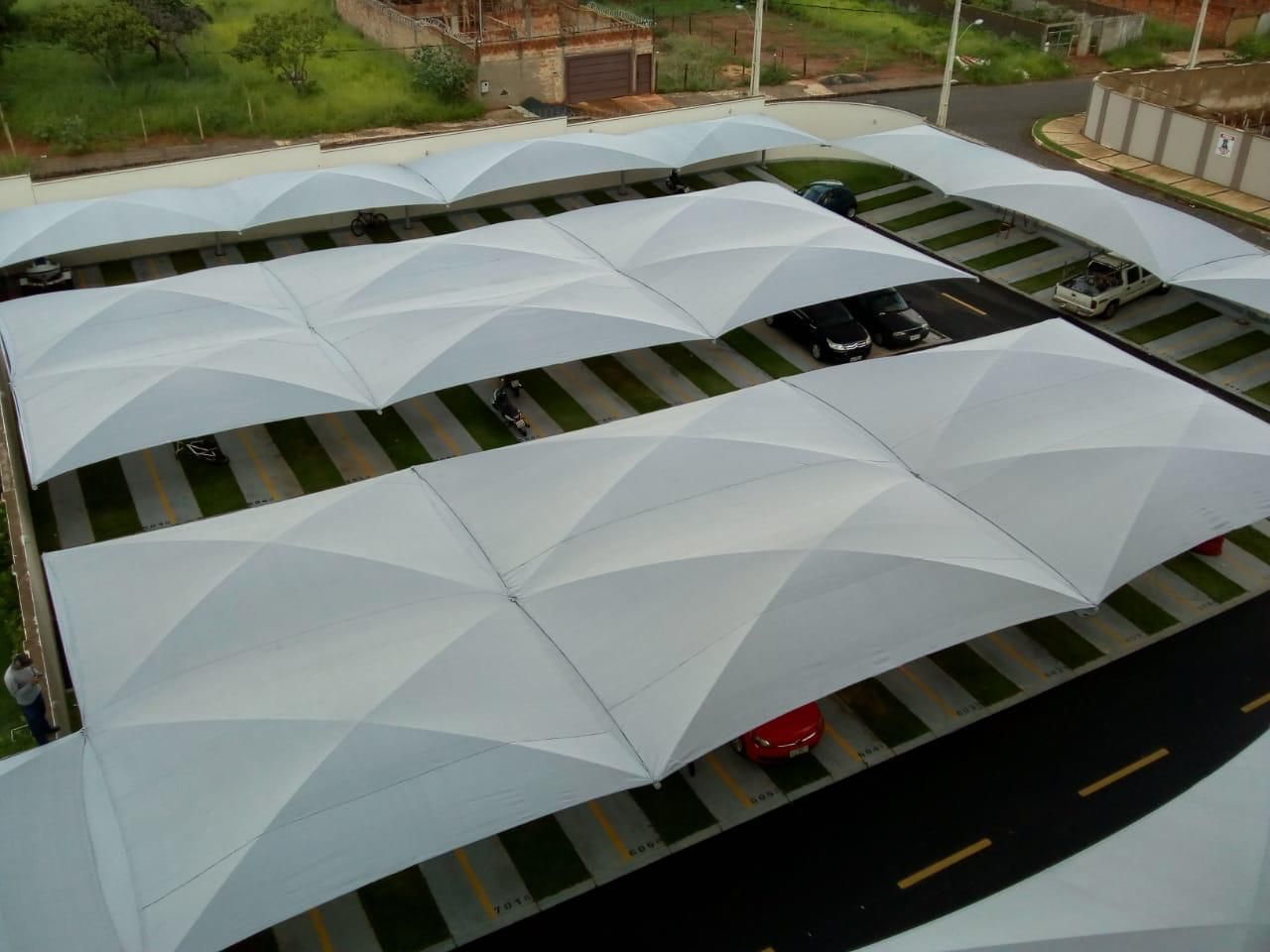 Uma vista aérea de um estacionamento com carros sob guarda-sóis brancos