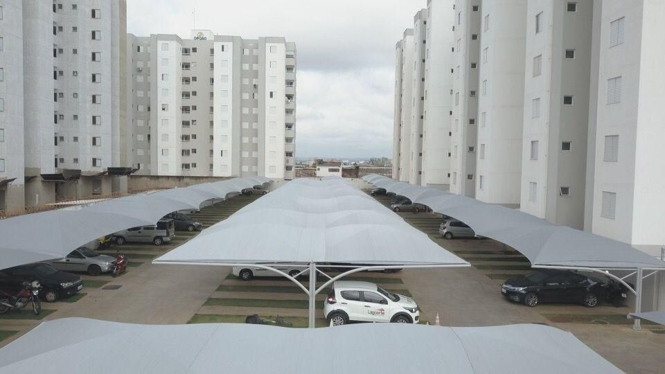 Muitos carros estão estacionados sob um guarda-chuva em um estacionamento.