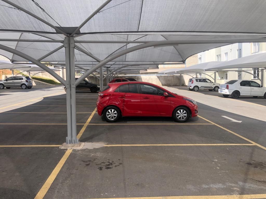 Um carro vermelho está estacionado sob uma marquise em um estacionamento.