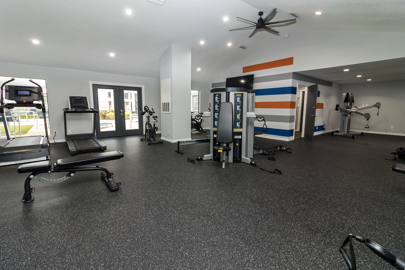 Gym with treadmills, weight machines, and free weights. Gray walls, black rubber flooring.