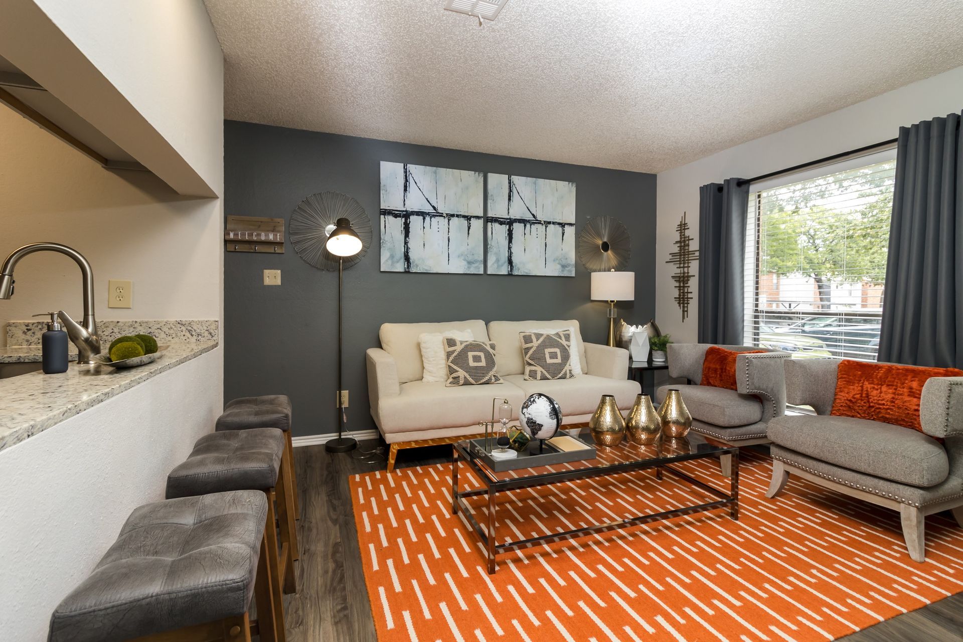 Living room with orange rug, grey couch and chairs, and artwork.