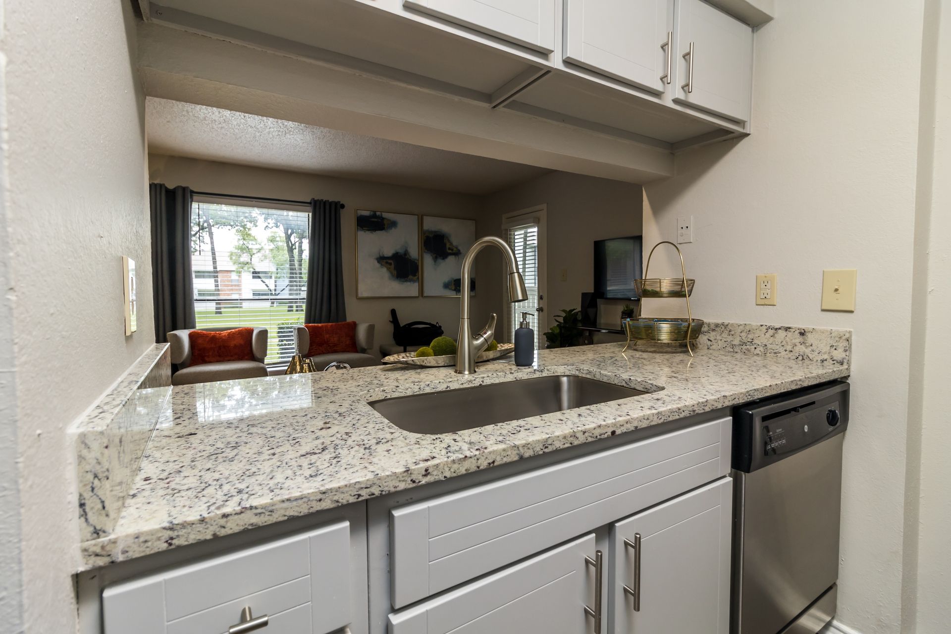 Kitchen with gray cabinets, granite countertop, stainless steel sink and appliances, and view of the living area.