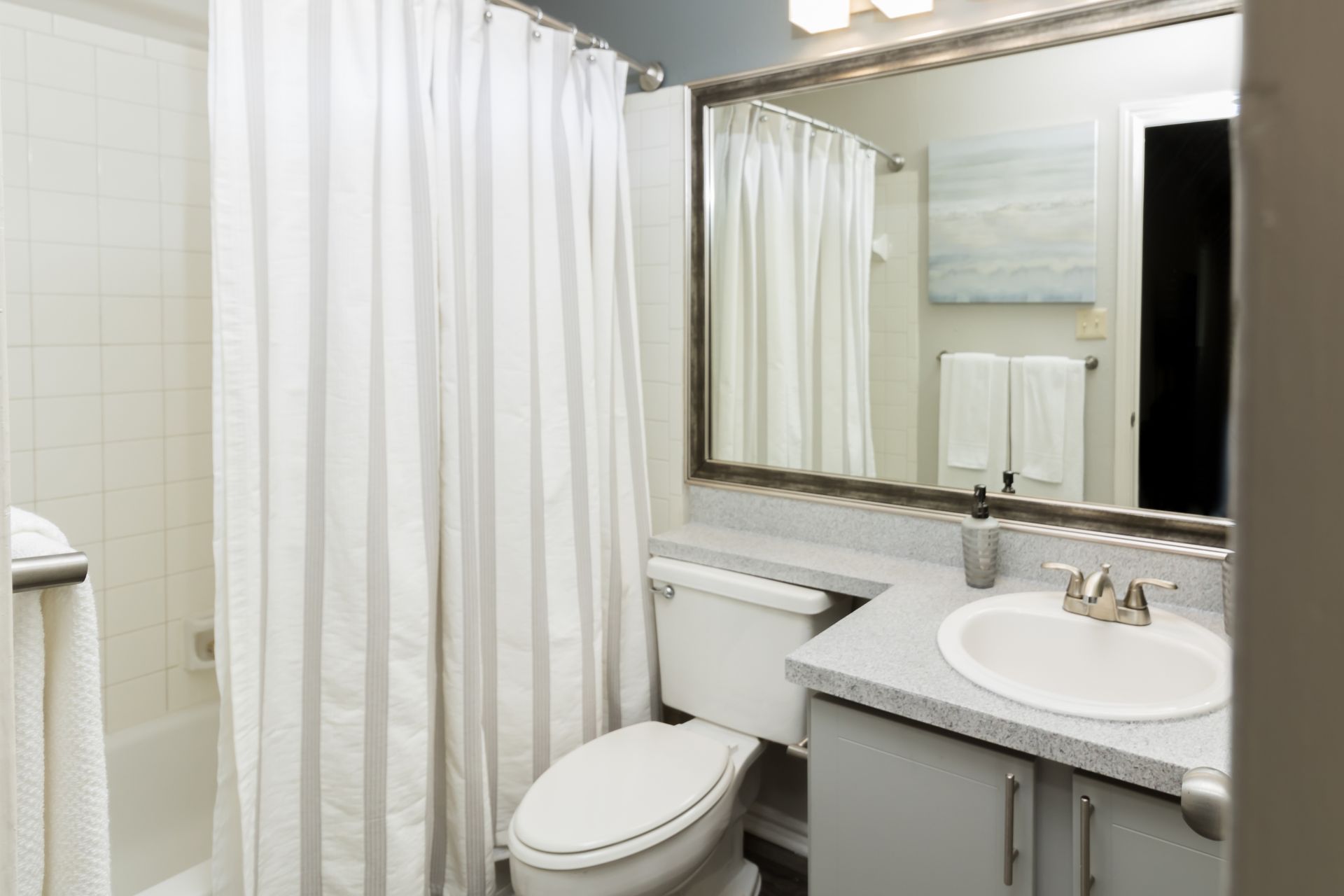 Bathroom with white and gray striped shower curtain, toilet, sink, and mirror.
