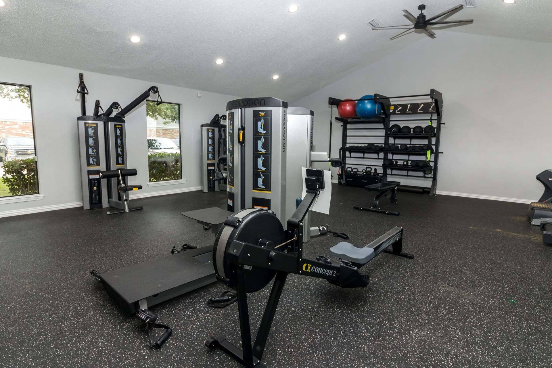 Gym interior with equipment, including a rowing machine, weight racks, and exercise machines.