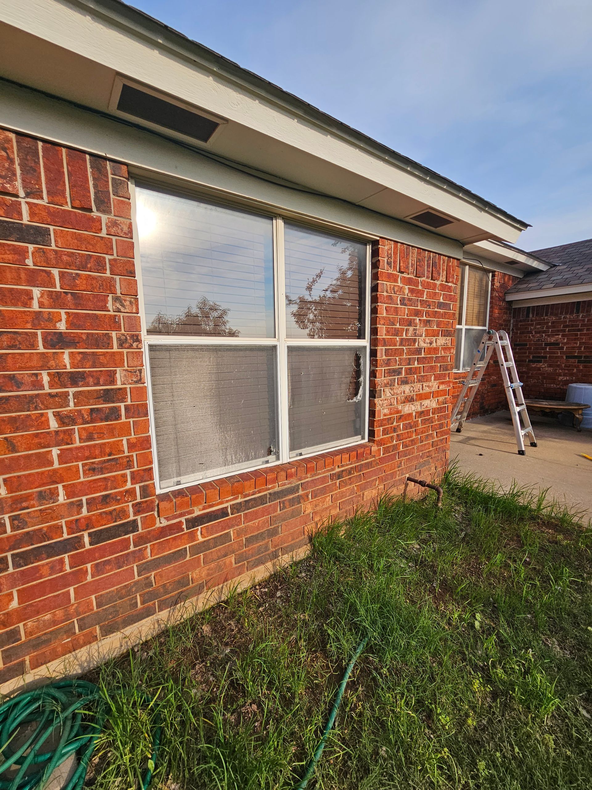 Brick house with window and a broken pane, ladder propped against the side.