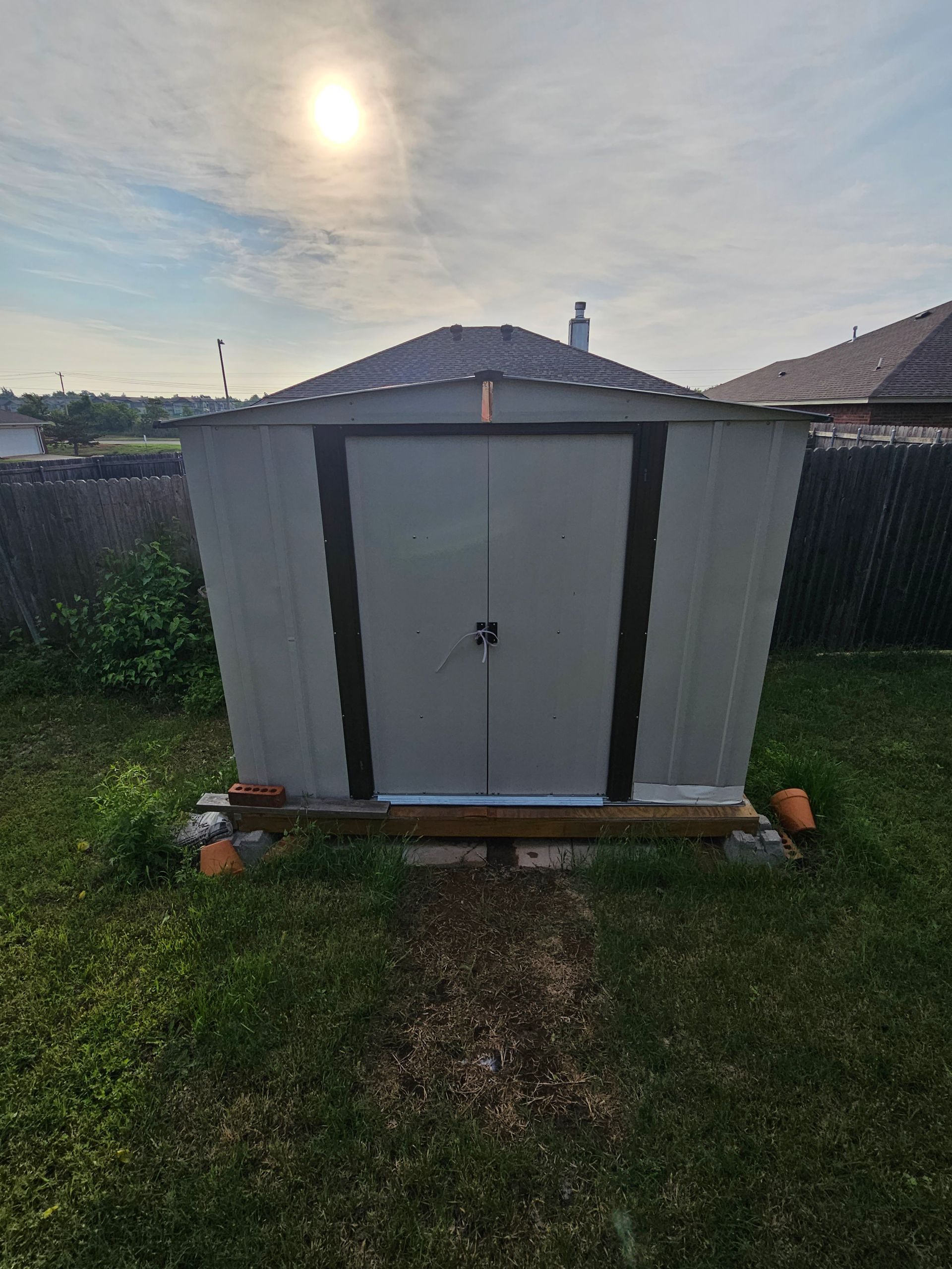 Gray metal shed with dark trim, in grassy backyard, under bright sky.