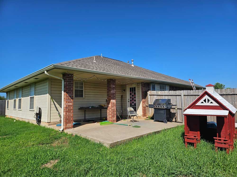Backyard with beige house, red brick pillars, grill, playhouse, and blue sky.