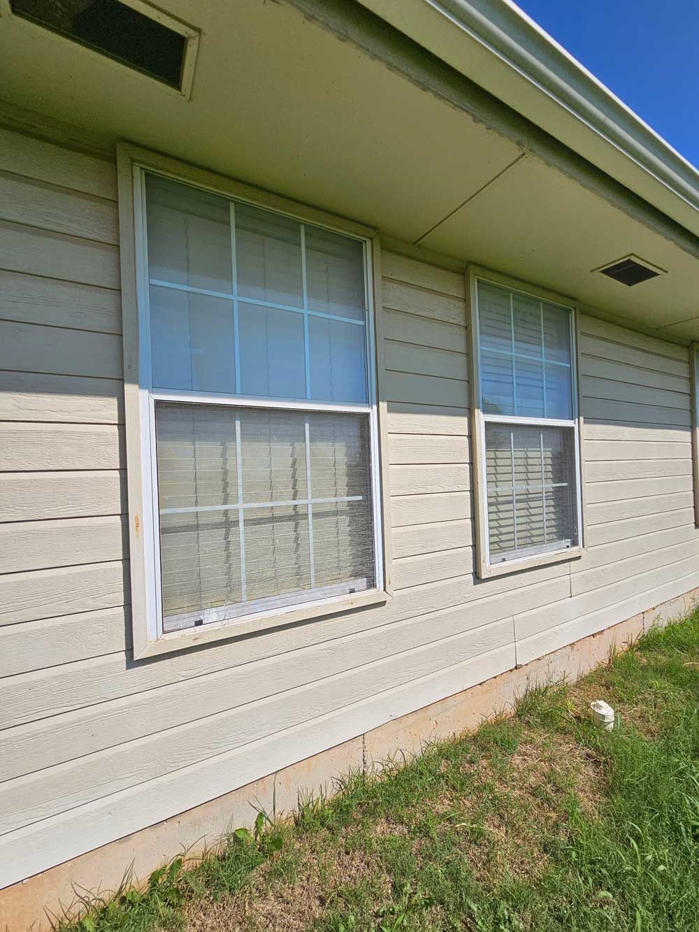 Two vertical windows on a light beige building with white frames; green grass below.