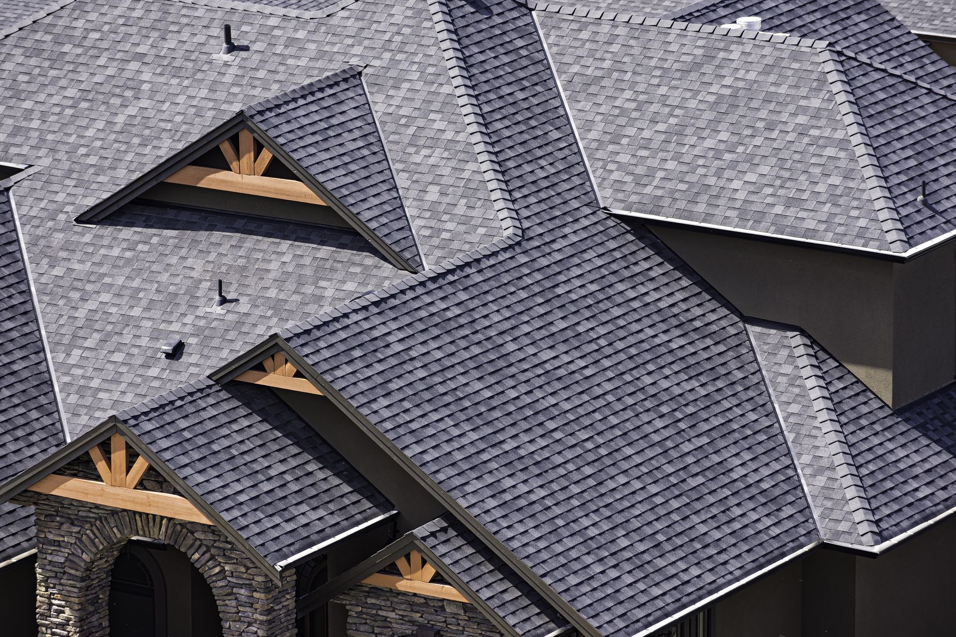 Gray shingled roof with wooden beams, dark blue shingles, and a stone facade.