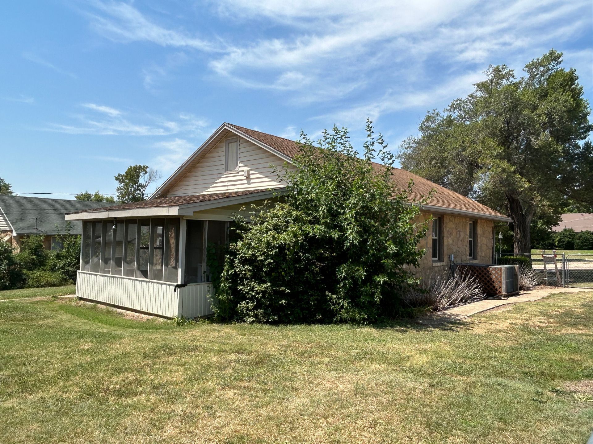 Small, light-colored house with a screened-in porch, set on a grassy lawn under a blue sky.