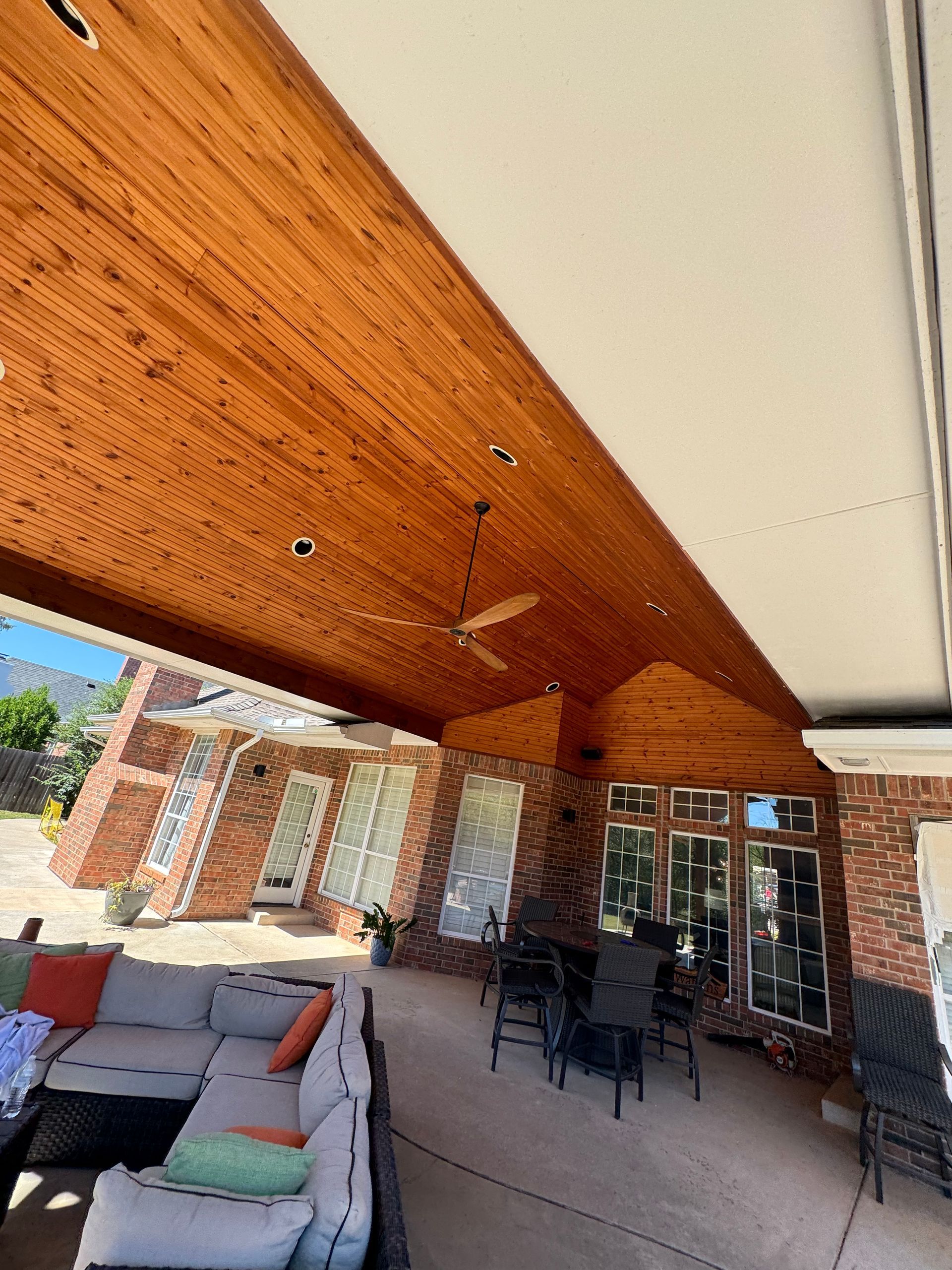 Outdoor patio with wood ceiling, seating, fan, and brick wall.