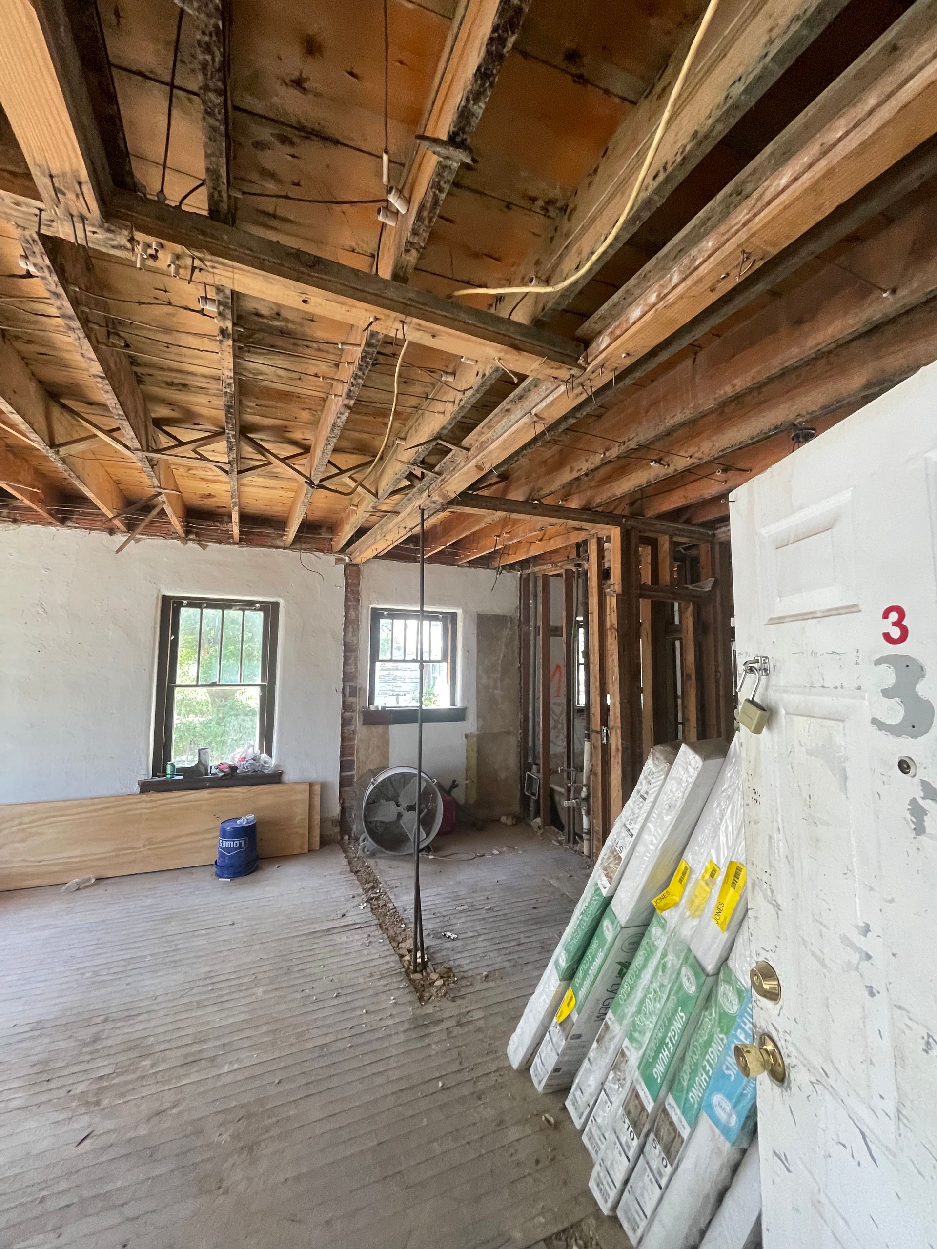 Interior of a room under renovation: exposed beams, unfinished walls, and materials stacked near a doorway.