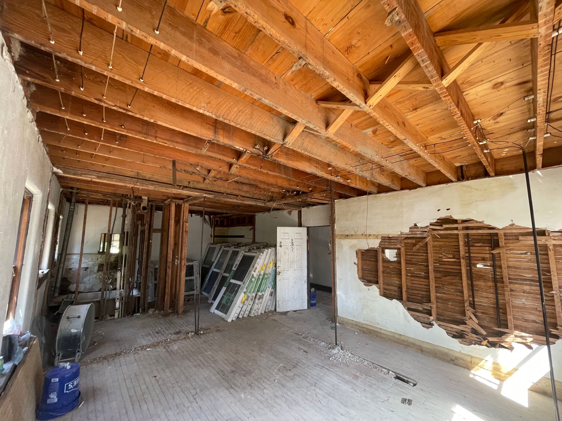 Interior of a room under renovation, exposed wood beams, debris, and construction materials scattered around.