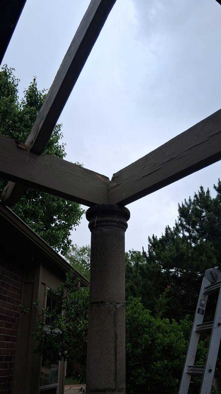 Pergola corner, wooden beams meet a stone column, overcast sky.