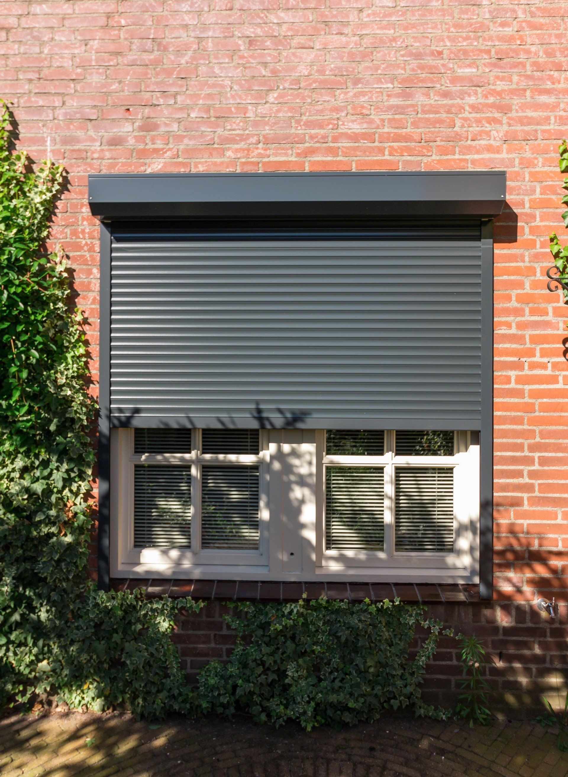 Een bakstenen gebouw met een raam met een grijs luik ervoor.