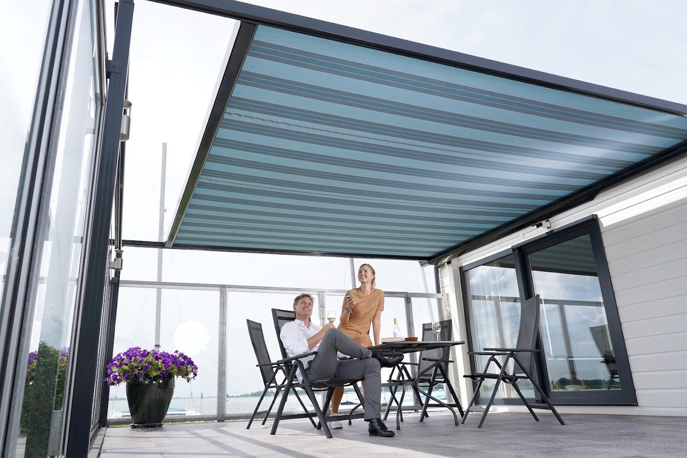 Een man en een vrouw zitten aan een tafel onder een luifel op een balkon.