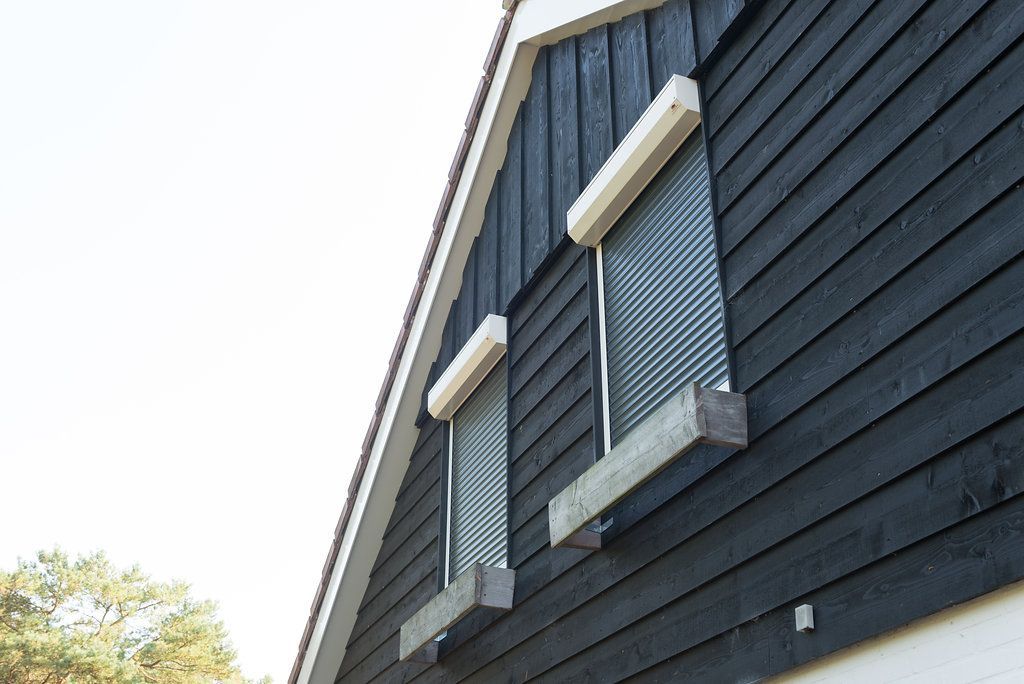 Twee ramen aan de zijkant van een huis met luiken ervoor