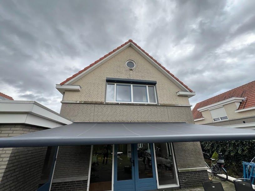 Een groot bakstenen huis met een blauwe deur en een grijze luifel.