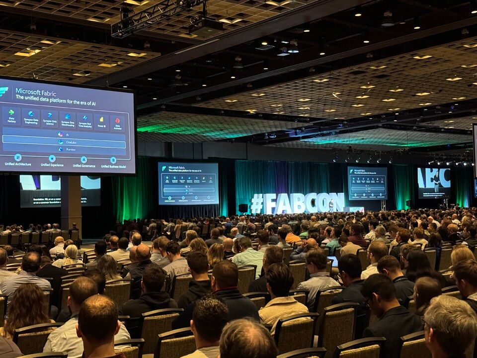 A large group of people are sitting in a conference room watching a presentation.