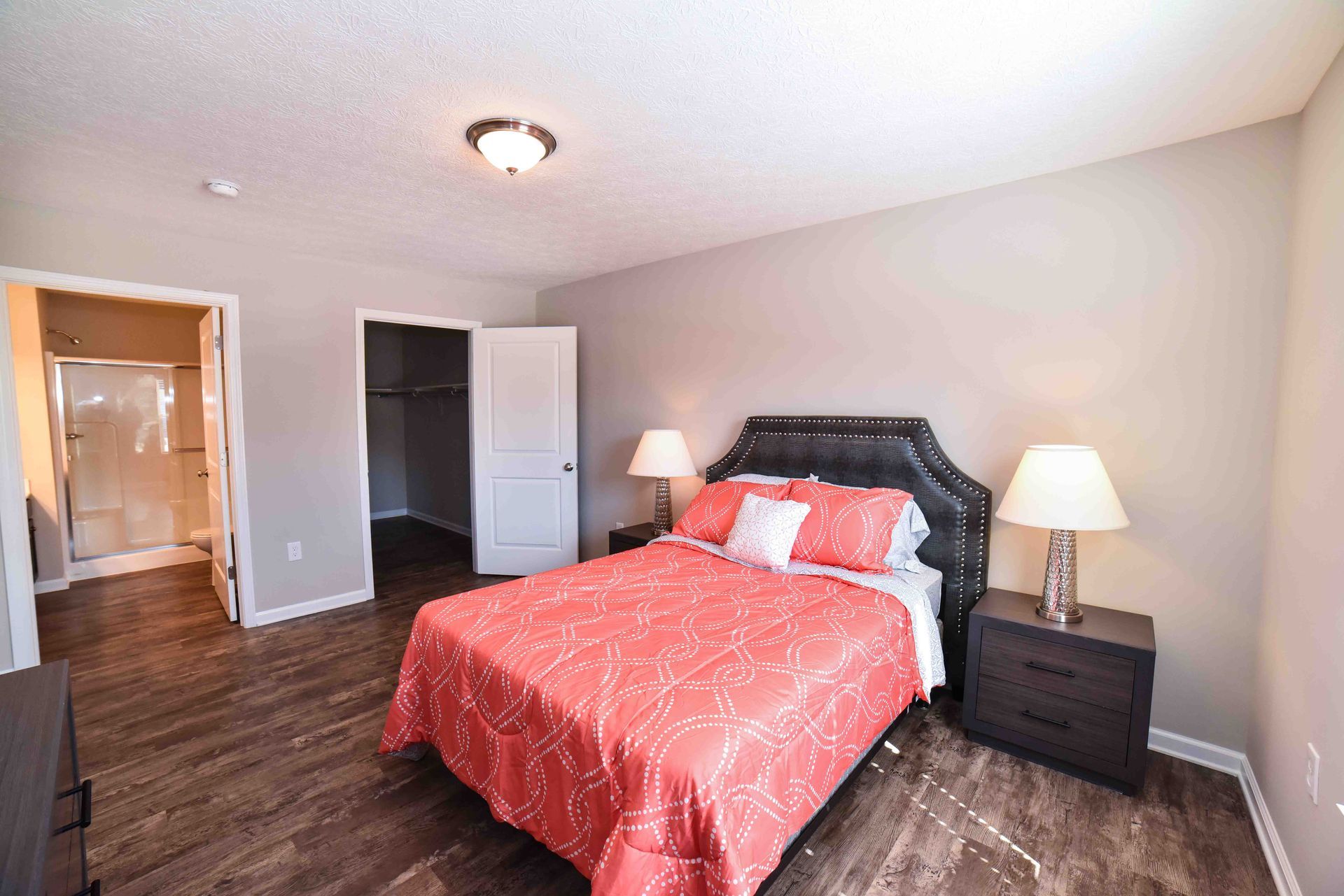 A bedroom with a bed , nightstands , lamps and a walk in closet.