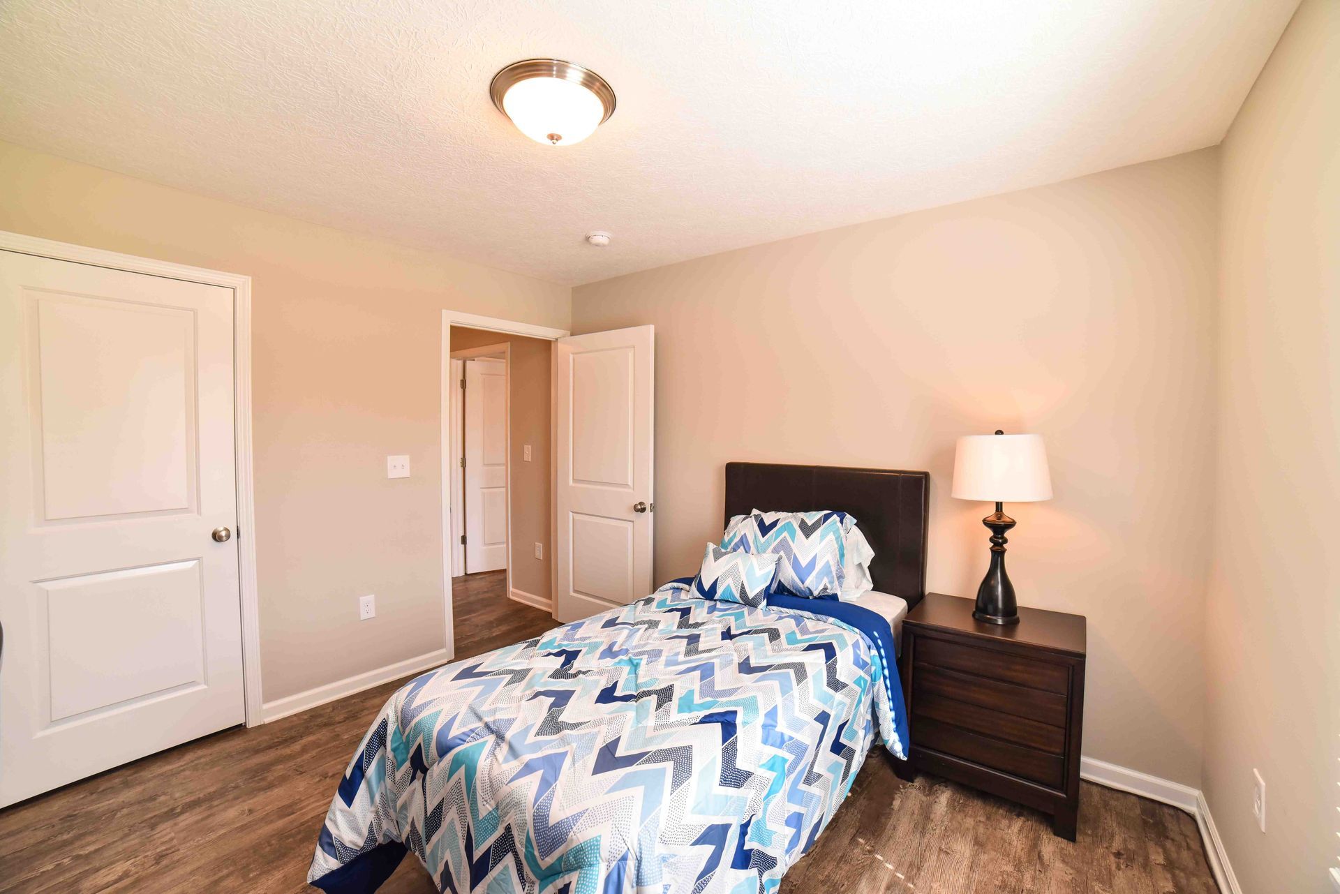 A bedroom with a bed , nightstand , lamp and closet.