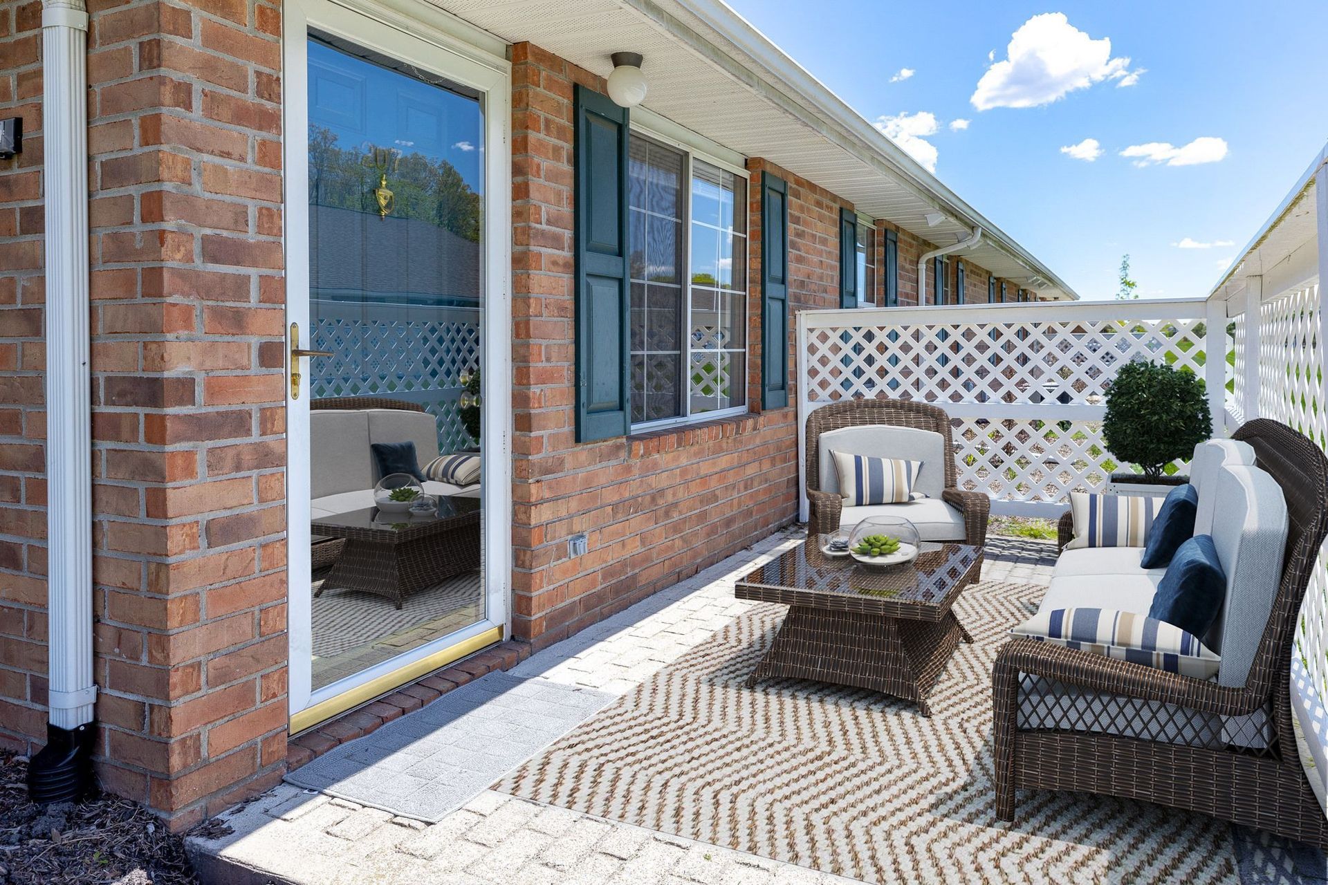 A patio with a couch , chair , table and rug in front of a brick house.