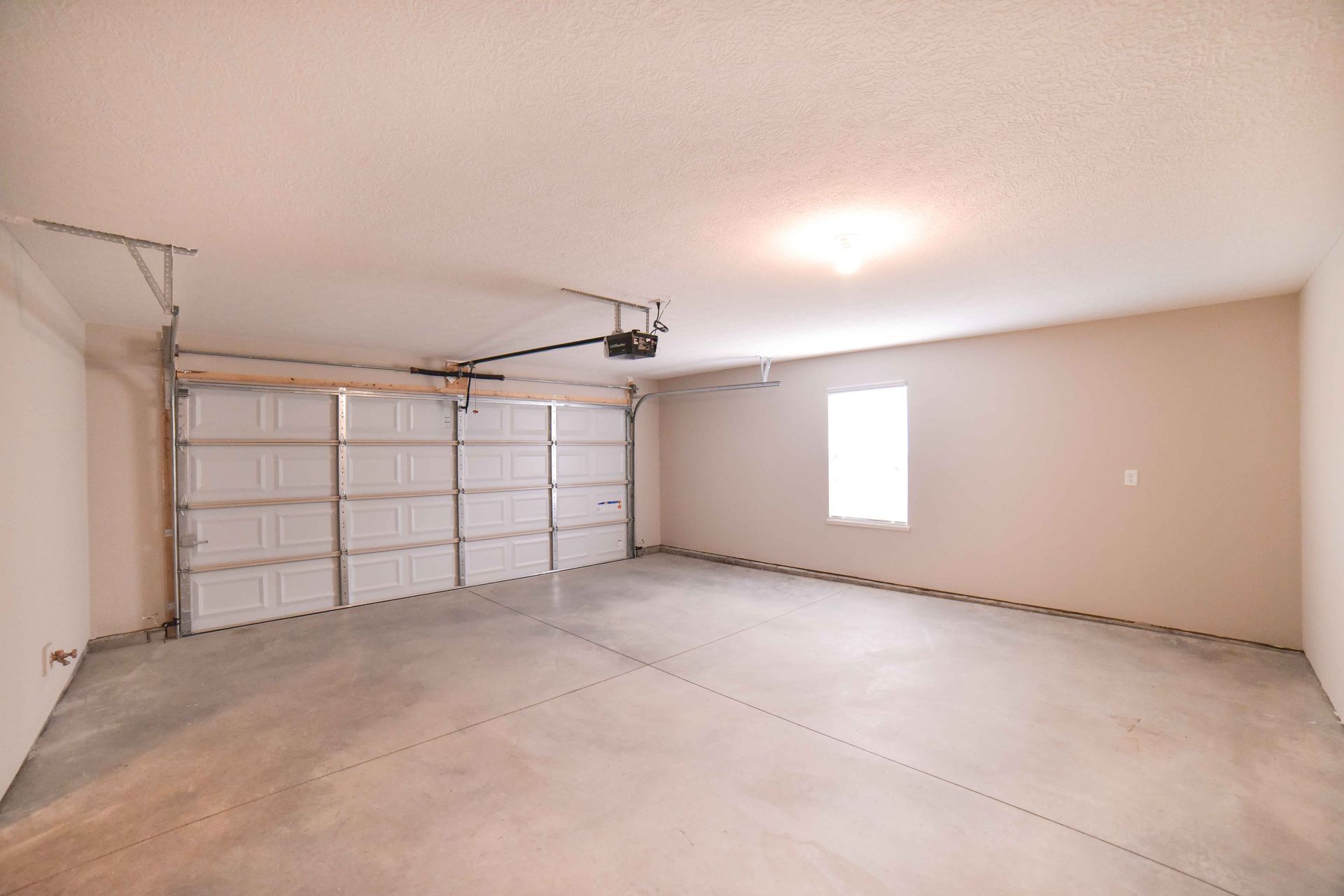An empty garage with a garage door open and a window.