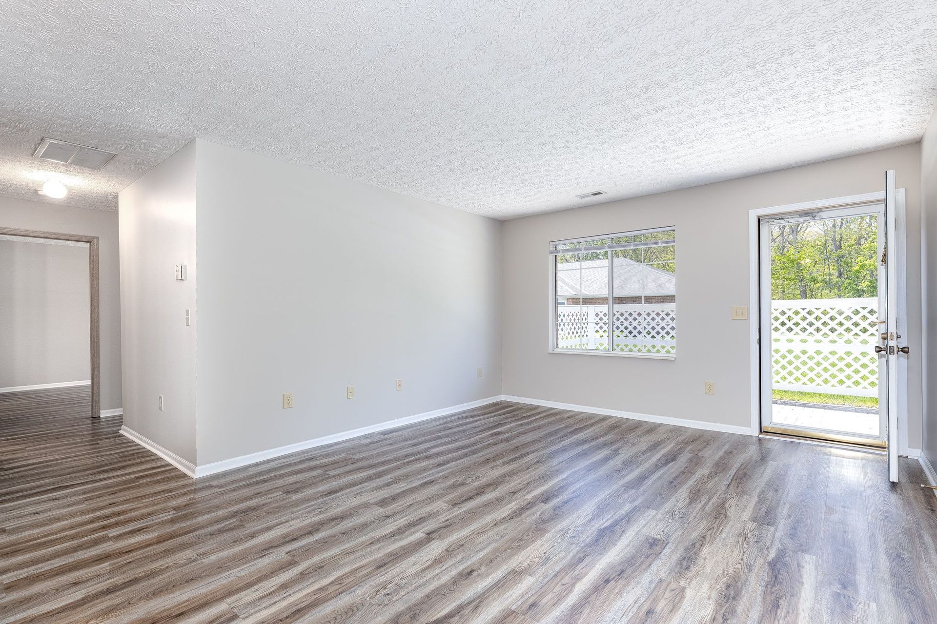 An empty living room with hardwood floors and a sliding glass door.
