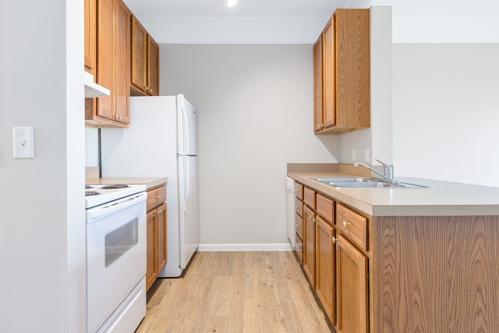 A kitchen with wooden cabinets , white appliances , a refrigerator and a sink.