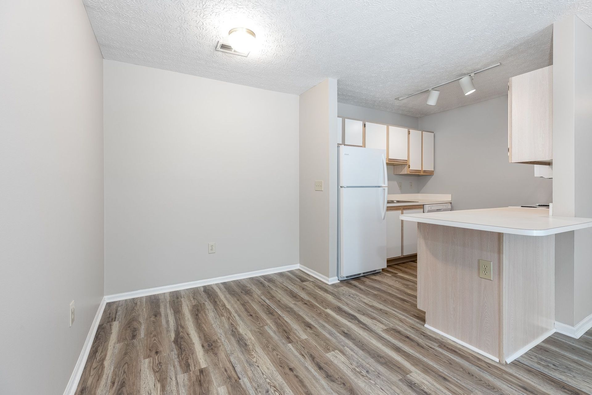 An empty room with a kitchen and a refrigerator in it.