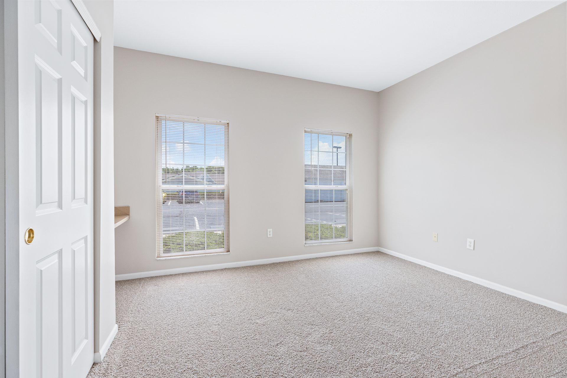 An empty bedroom with two windows and a carpeted floor.