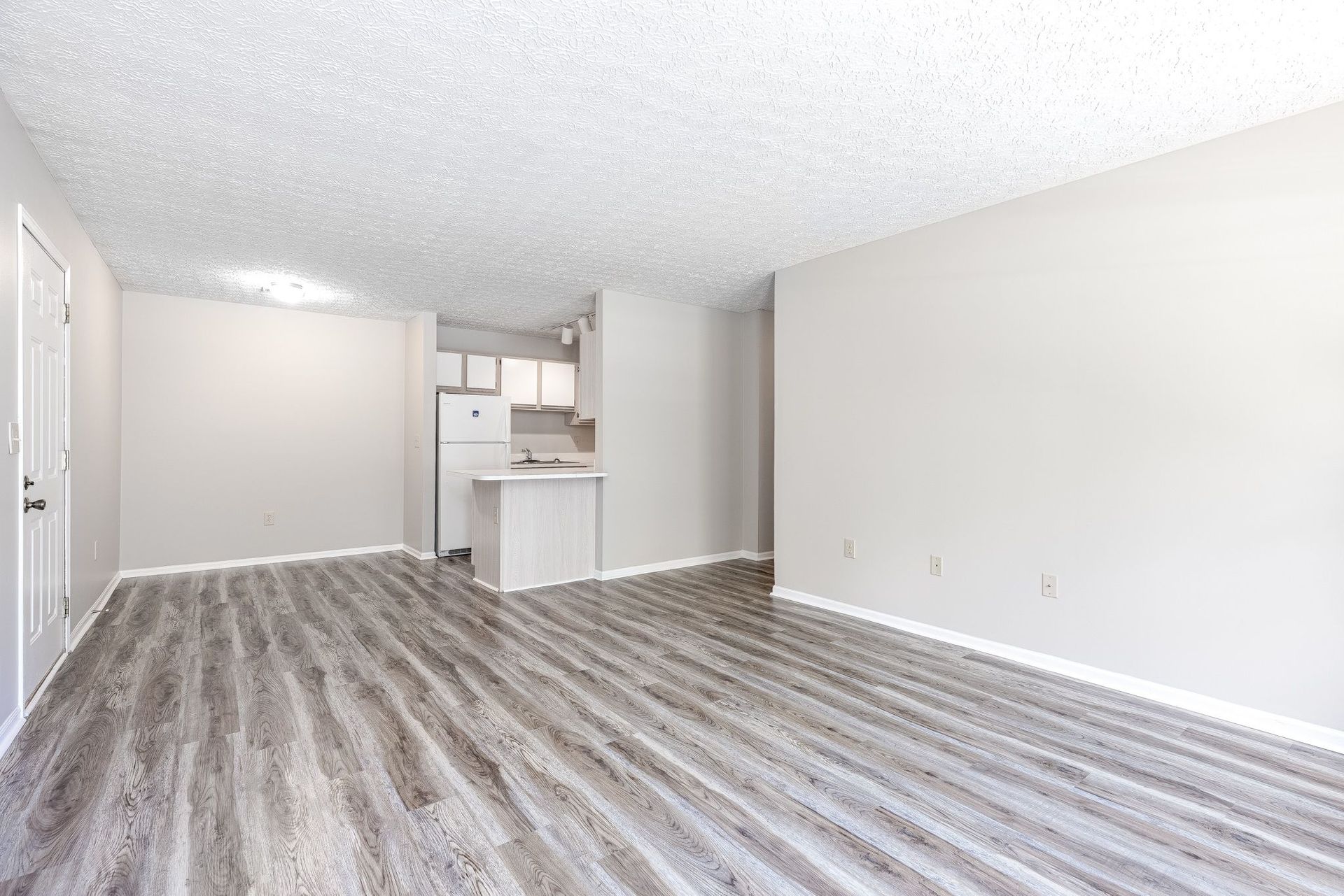 An empty living room with a wooden floor and white walls.