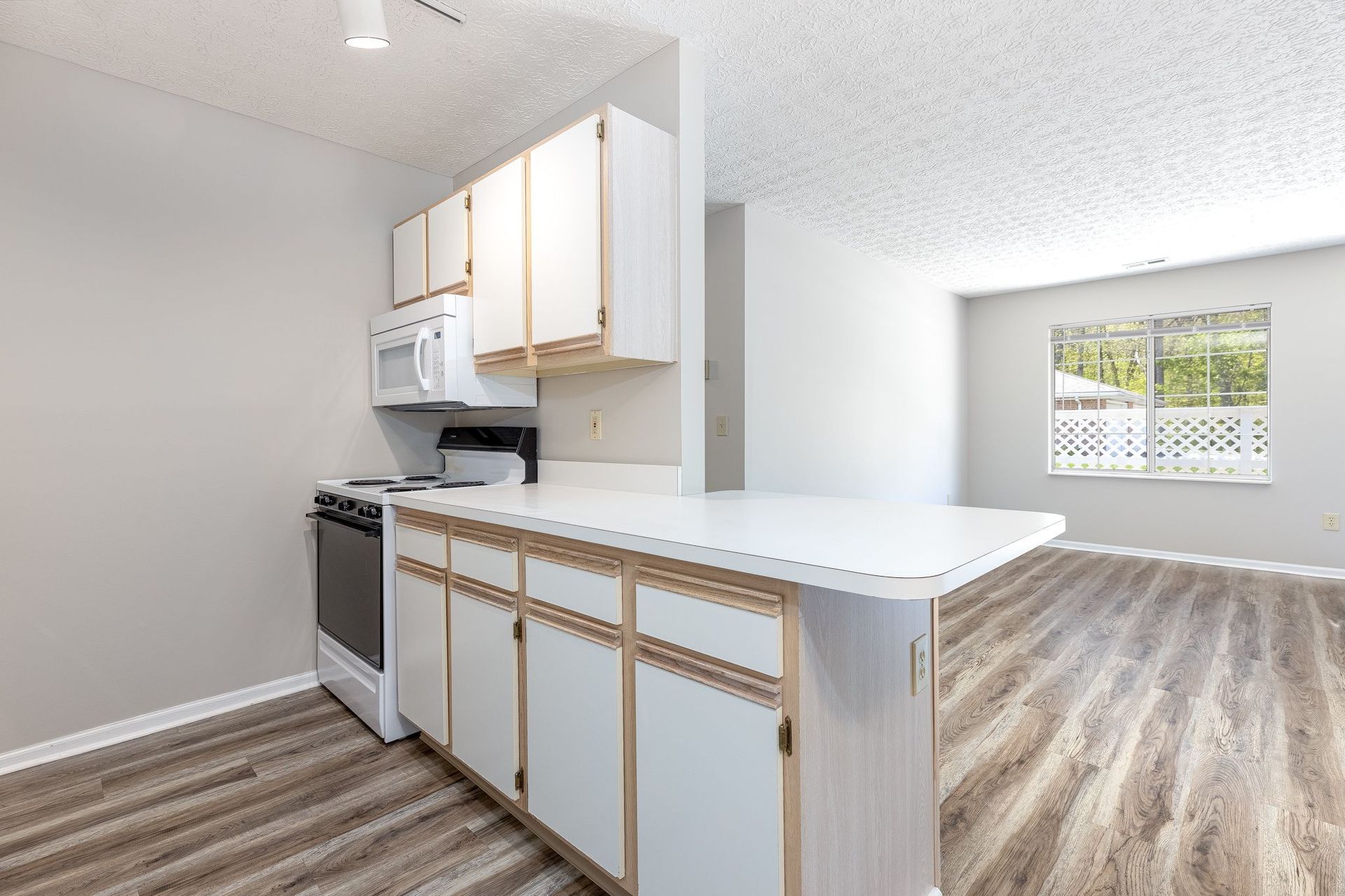 A kitchen with white cabinets , a stove , microwave , and hardwood floors.