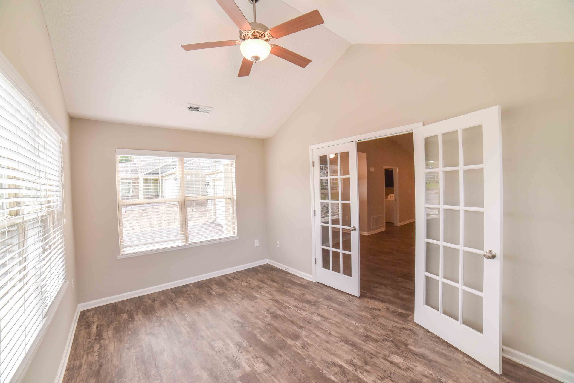 An empty room with a ceiling fan and french doors.