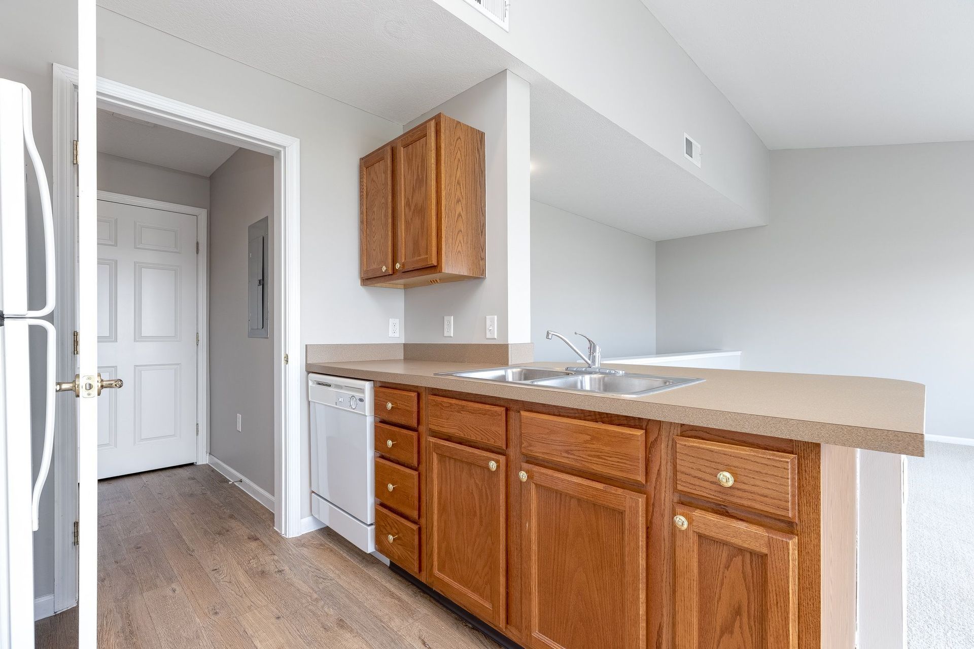 A kitchen with wooden cabinets , a refrigerator , a sink , and a dishwasher.