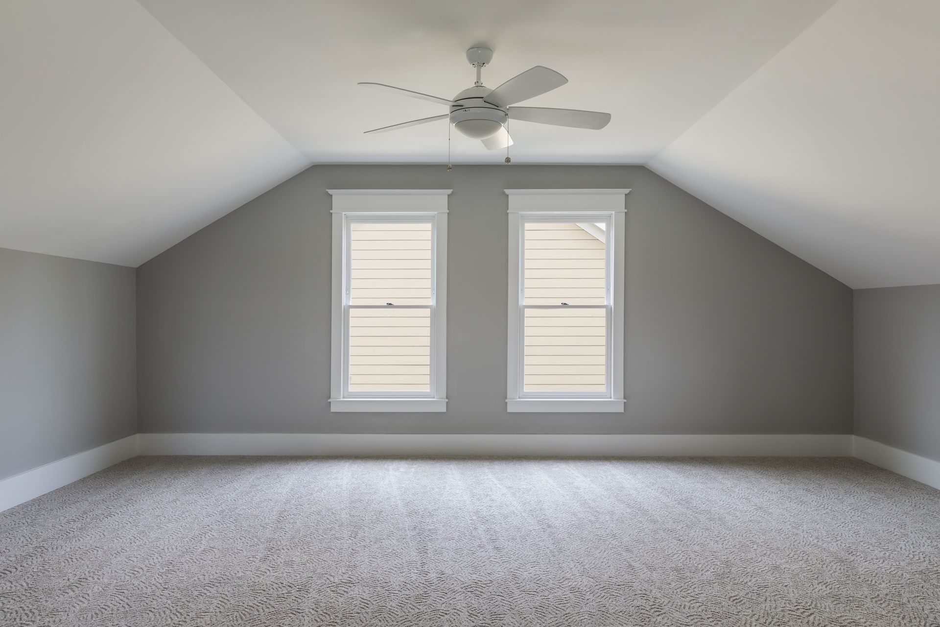 Empty room with gray walls, two windows, ceiling fan, and beige carpet.