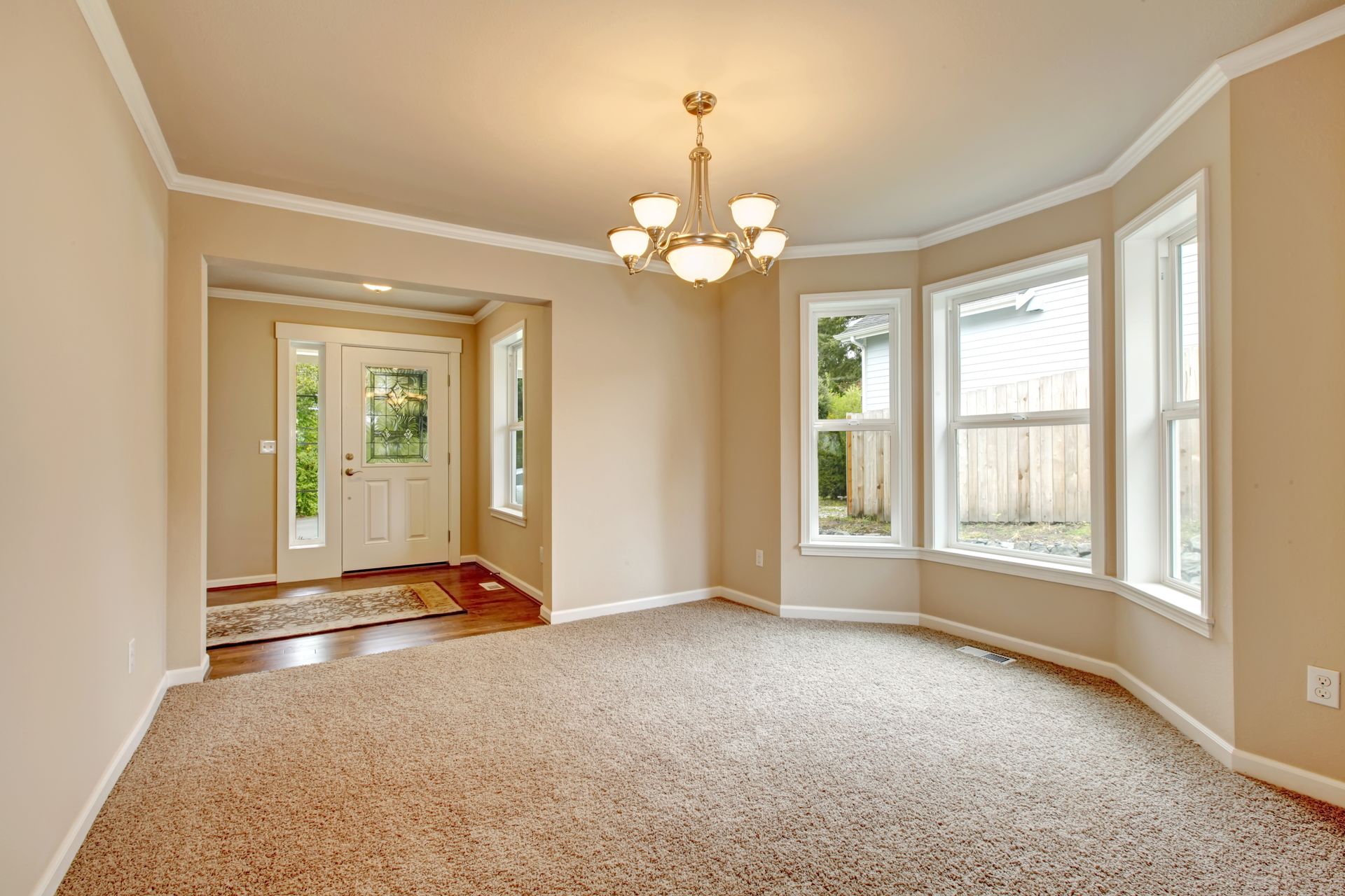 Empty living room with beige walls, carpet, and a bay window.