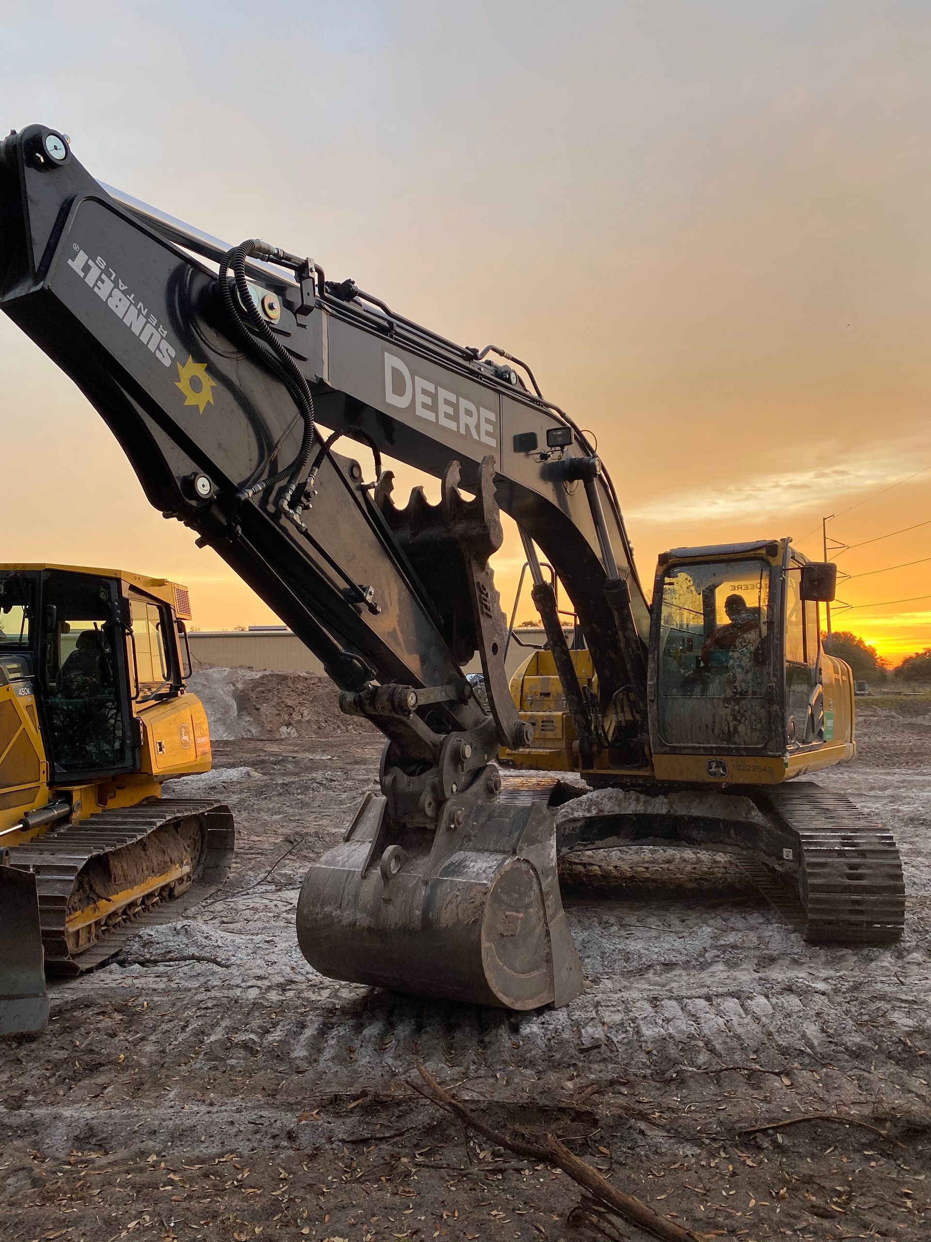 John Deere excavator on a muddy construction site at sunset.