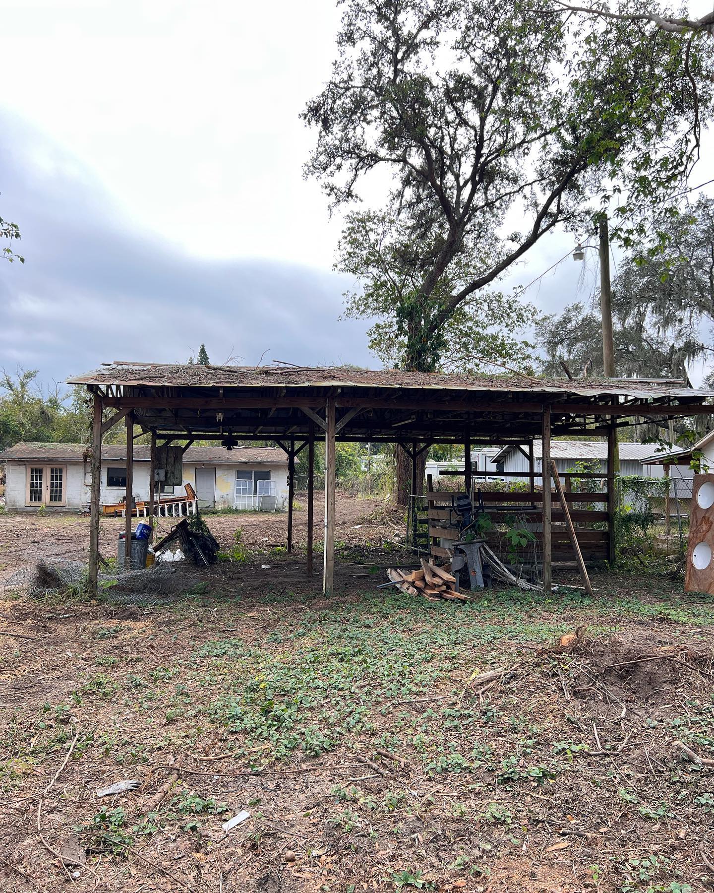 Dilapidated shed in a yard, with a house visible in the background under a cloudy sky.
