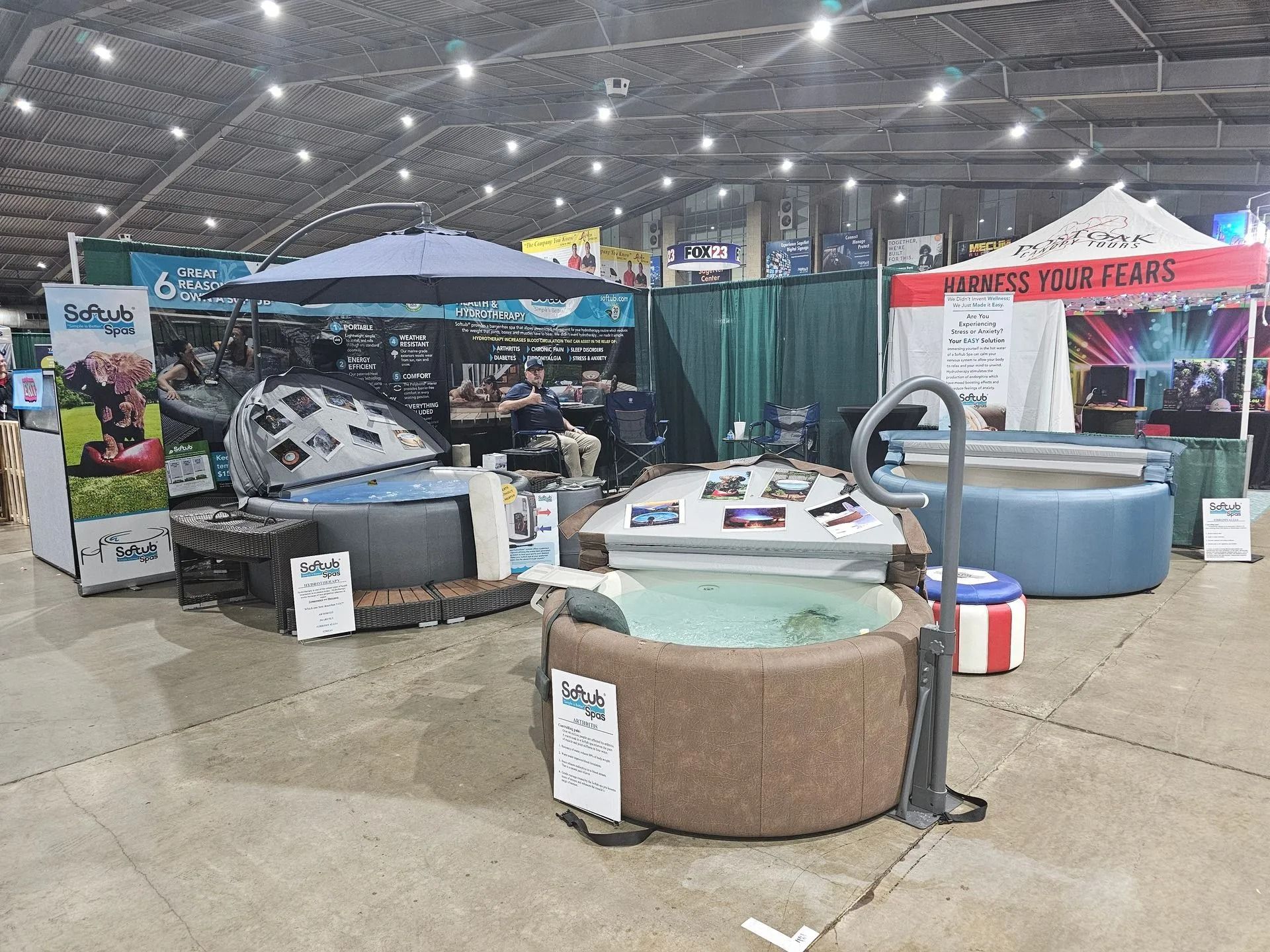Trade show booths displaying hot tubs. Indoor setting with various models and promotional materials.