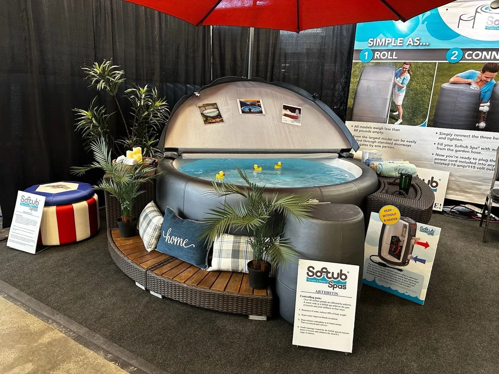 A hot tub display at a show. Features a round, inflatable tub with plants, pillows, and marketing materials.