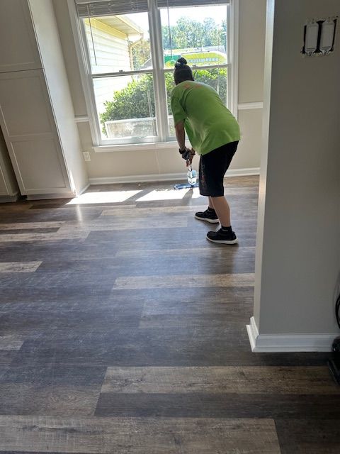 Person cleaning floor near window in room with laminate flooring.