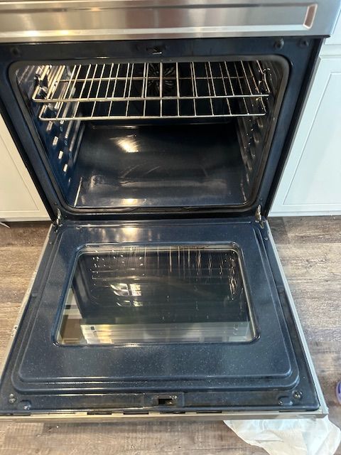 Open stainless steel oven, empty, with rack, in a kitchen setting.