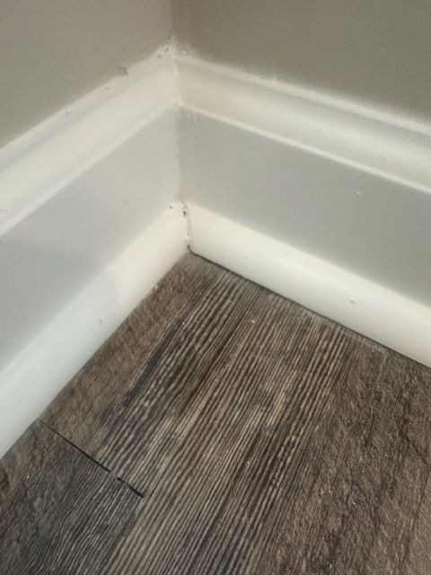 White baseboards meet at a corner on a wood-look floor, a gray wall above.