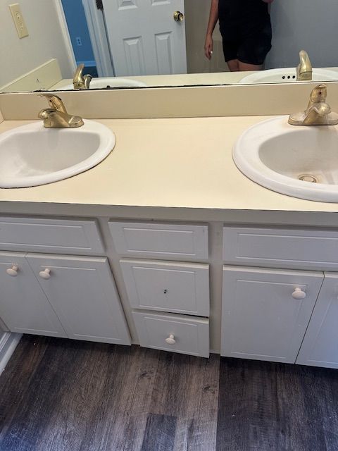 Bathroom with double sinks, white cabinets, and a light-colored countertop. Faucets are gold.