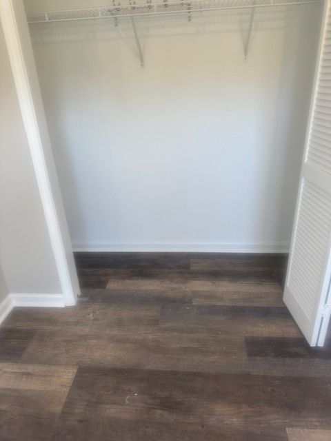 Empty closet with white walls, a wire shelf, and dark wood-look flooring.