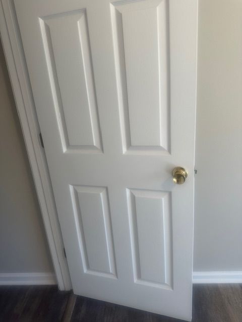 White, four-panel interior door with gold doorknob, in a room with light walls and wood-look flooring.